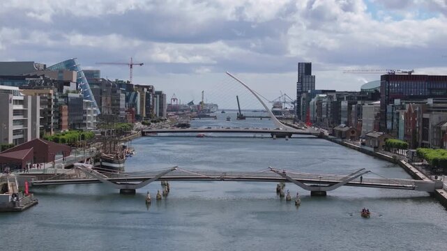 Central waterway leads toward Samuel Beckett and Sean O&rsquo;Casey bridges amid glass-fronted docklands offices and moving small boats.