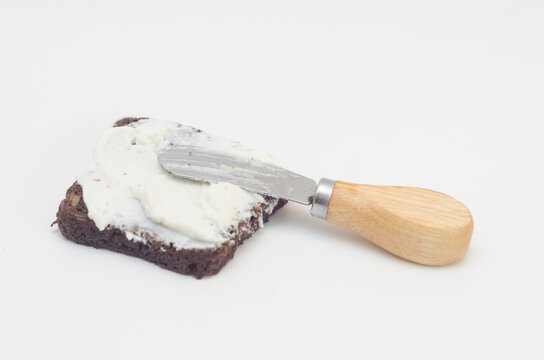 Ricotta cheese spread on a slice of brown bread and butter knife on white background.