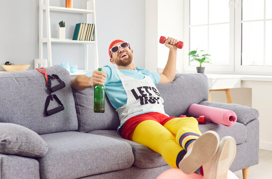 Lazy and funny man in sportswear is sitting on the couch, sipping wine during workout at home gym. Relaxation and indulgence, blending the worlds of fitness and alcohol in an unexpected way.