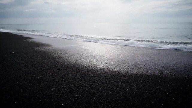 Waves rolling onto dark volcanic sand beach at overcast coastline ocean sea coast water shore ocean sea coast water