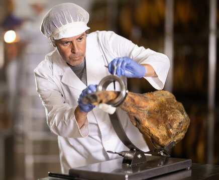 Male worker places jamon on jamonero to cut it into appetizing pieces. Ham factory