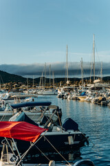 Fototapeta premium Boats and masts fill a calm marina basin under a clear blue sky with hills beyond. Boating leisure and marina infrastructure appealing to summer travel and watersport tourism