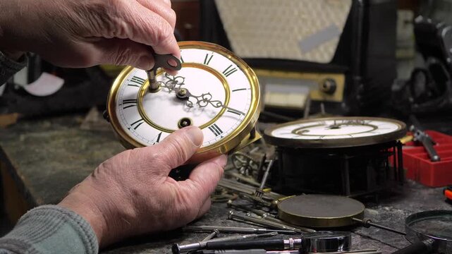 An elderly craftsman, in a workshop, repairs an old clock mechanism, an antique watch, adjusts gears, lubricates them with oil, cleans them from dust and dirt. Slow motion.
