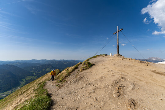 Hiker ascending trail to mountain summit cross on Fellhorn Germany