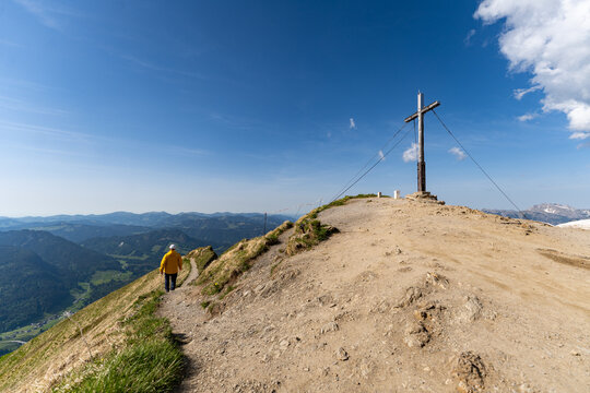 Hiker on Fellhorn mountain peak path near summit cross, Germany.