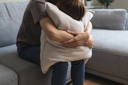 Unhappy anxiety young Asian woman covering her face with pillow on the cough in the living room at home.
