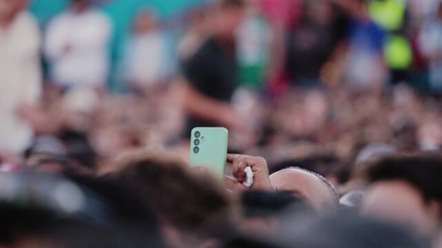 Crowd of spectators at soccer championship event with fans raising smartphones to capture moments, vibrant background colors enhancing the lively atmosphere