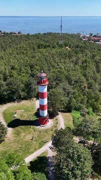 Vertical aerial drone view of Nida lighthouse on the Curonian Spit, Lithuania. Portrait summer landscape of Baltic landmark surrounded by pine forest with Curonian Lagoon on the horizon.