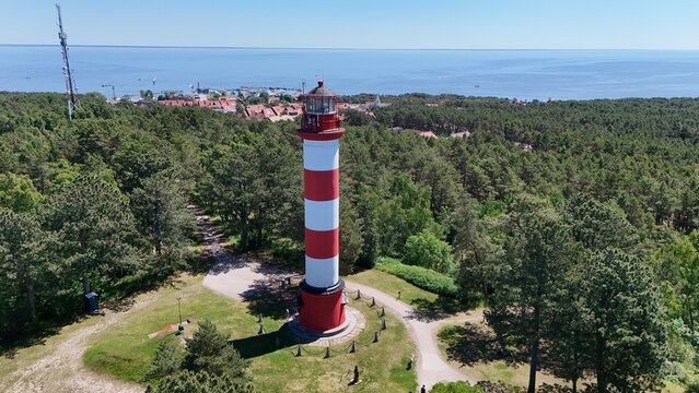 Aerial view of Nida lighthouse surrounded by lush pine forest in Curonian Spit national park, Lithuania. Scenic summer landscape with Baltic Sea coast and historic red and white beacon.