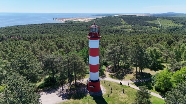 Aerial panorama of Nida lighthouse nestled in the pine forest of Curonian Spit, Lithuania. Beautiful summer landscape with Baltic Sea, coastal lagoon, and historic red and white beacon.