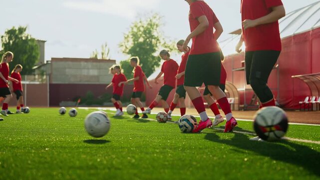 Young womens soccer team practicing coordinated ball control drills on a sunny artificial turf field during structured outdoor training session
