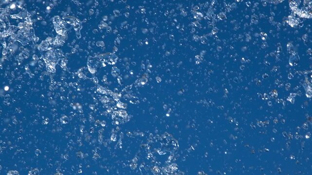 Close-up of sparkling fountain water splashes against clear blue sky. Refreshing droplets create dynamic abstract background representing freshness, summer, energy and motion