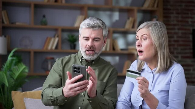 Close up of upset senior married couple facing fraud problem using credit card and smartphone at home, shocked after discovering banking issue and possible financial loss and transaction error.