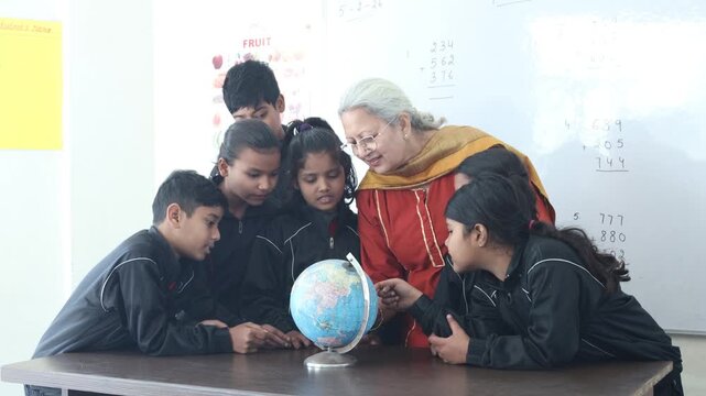Senior indian teacher explaining geography concepts, pointing at globe with children as they engage learning activity during a school lesson, Education india.