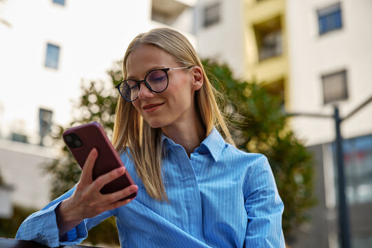 Smiling urban woman using smartphone outdoors wearing glasses