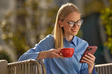 Young woman enjoying coffee and smartphone outdoors