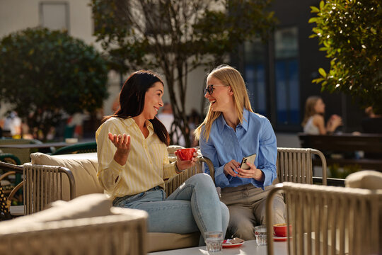 Female friends laughing enjoying coffee at outdoor cafe