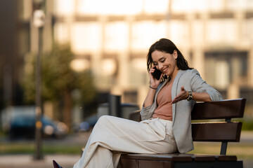Fototapeta premium Businesswoman talking on phone sitting on park bench