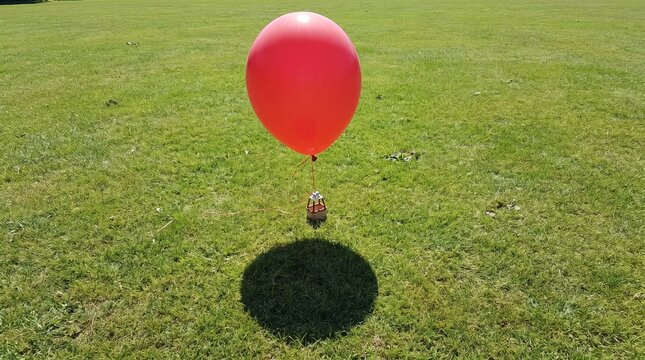 Bright red balloon floating above grassy field with distinct shadow with outdoor