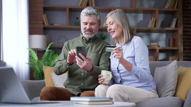 Senior married couple using a mobile phone and credit card for online shopping at home. Retired husband and wife browsing products, making digital purchases and satisfied with their buying decisions.