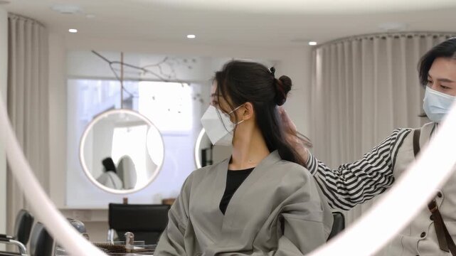 Man hairdresser stylist making curls hairstyle with curling iron and make wave for long hair of the female customer with silk robes in modern spa hair salon care service for a stylish transformation
