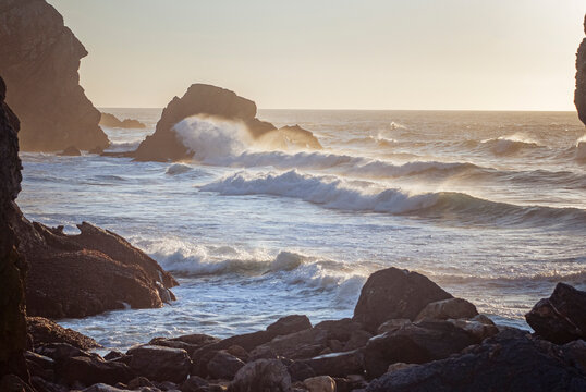 Praia da Ursa, Portugal: Ocean waves crashing against rocks on a coastline at sunset