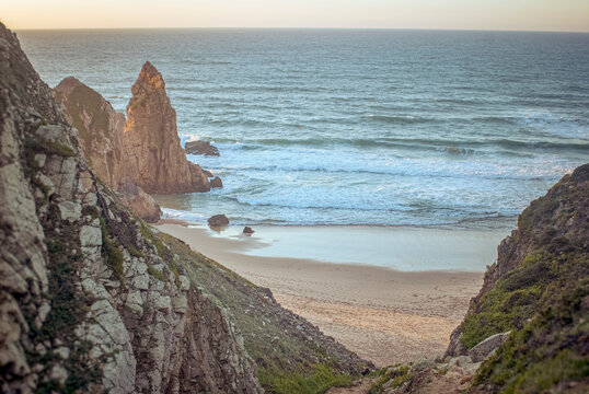 Praia da Ursa, Portugal: Rocky coastline with sea stack beach and ocean waves at sunset