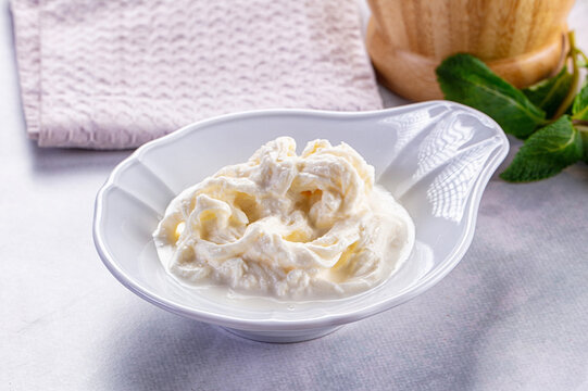 Creamy stracciatella cheese in white ceramic bowl with mint leaves and linen napkin
