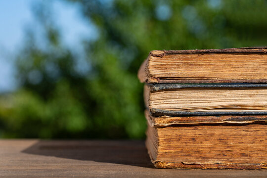 Closeup of weathered ancient books stacked on wood surface with blurred green nature background and copy space for education literature history and lifestyle concepts