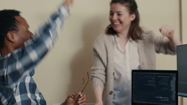 System engineer celebrates successful code compiling with a high five at a multiple monitor desk, showing teamwork, debugging success and project progress