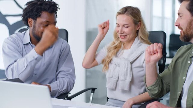 Multiethnic business team three diversity business colleagues happy playing rock paper scissors game with hands laughing having fun Caucasian businessman winning flick coworkers on foreheads in office