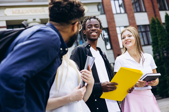 Group of diverse university students sharing a happy moment, smiling and communicating outdoors on campus with books