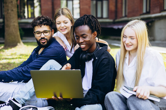 Group of diverse college students studying and working together outdoors on a laptop, sharing ideas and smiling