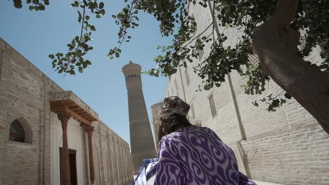 A young woman with long hair in an oriental robe and a skullcap walks through an ancient oriental city