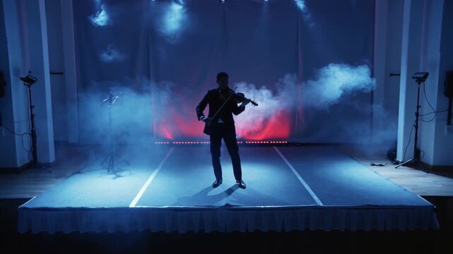 Adult male violinist bowing on small hall stage after lighting cue, with violin, bow and fog