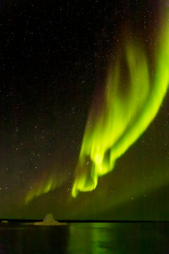 Bright green aurora stretches across the sky and reflects on the water in Greenland