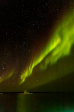 Brilliant green northern lights dance over an iceberg under a starry sky in Kalaallit Nunaat, Greenland