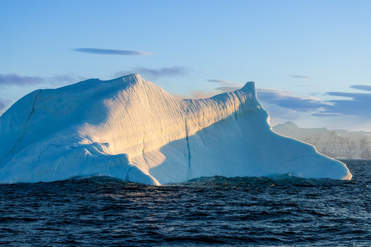 Golden sunrise light on a sculpted iceberg with soft clouds near Ittoqqortoormiit in Greenland