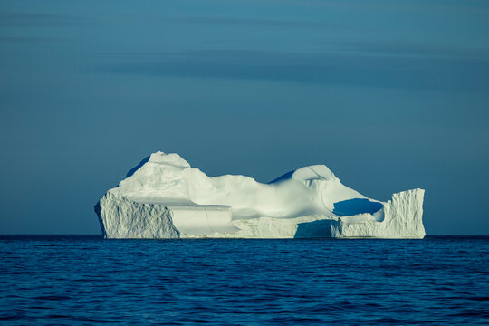 Large flat-topped iceberg floats in blue seas under pastel sky near Ittoqqortoormiit, Greenland