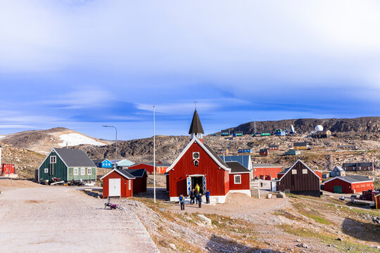 Red church and colorful houses in Ittoqqortoormiit, Greenland, show life in one of the world's most isolated towns during a sunny day