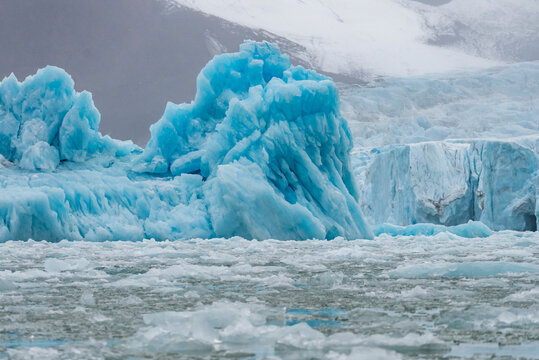 Jagged blue iceberg rises from broken ice sea in Greenland with dark mountains in background