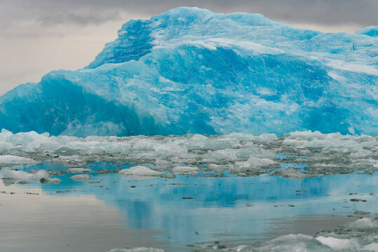 Luminous blue iceberg rises above cracked sea ice reflecting in still water in Greenland's icy landscape