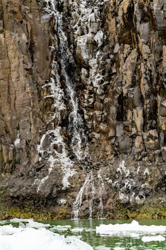 Waterfall flows between basalt columns with snow in Borgvig Greenland