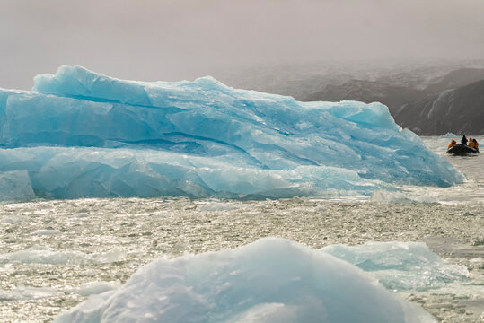 Fractured blue ice rests on water under soft Arctic haze in the area of Borgvig in Greenland