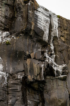 Basalt cliff displaying layered icicles and rock patterns in Arctic landscape