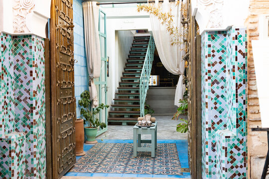 Interior view of a riad in Morocco featuring traditional tile work, a staircase, and plants in natural light