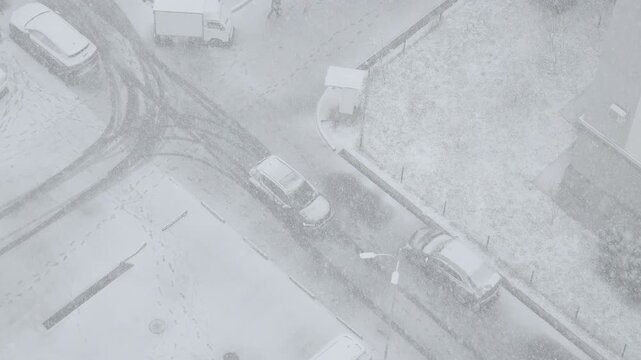 Aerial top-down view tracking a moving car on a snowy city street. Surveillance camera perspective of winter driving conditions in slow motion.