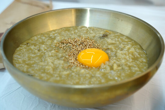 Korean abalone porridge topped with raw egg yolk and sesame seeds in a traditional brass bowl.
