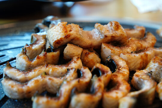 Fresh raw fresh water eel fillets grilling on a hot charcoal barbecue gridiron plate in a restaurant