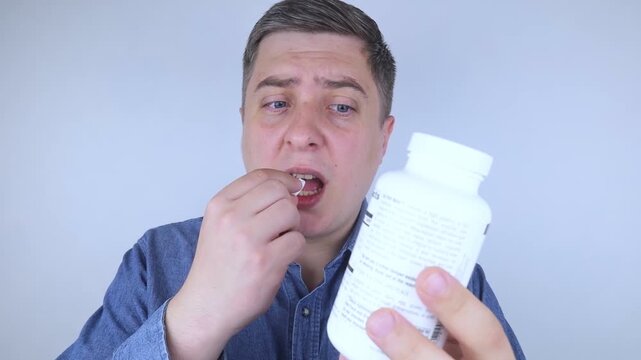 Man suffering from phagophobia struggling to swallow pill. Caucasian male looking anxious and scared before taking medication, experiencing fear of choking or swallowing difficulties.
